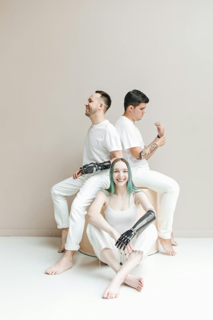 Studio photo of three adults with prosthetic arms sitting together in white attire.