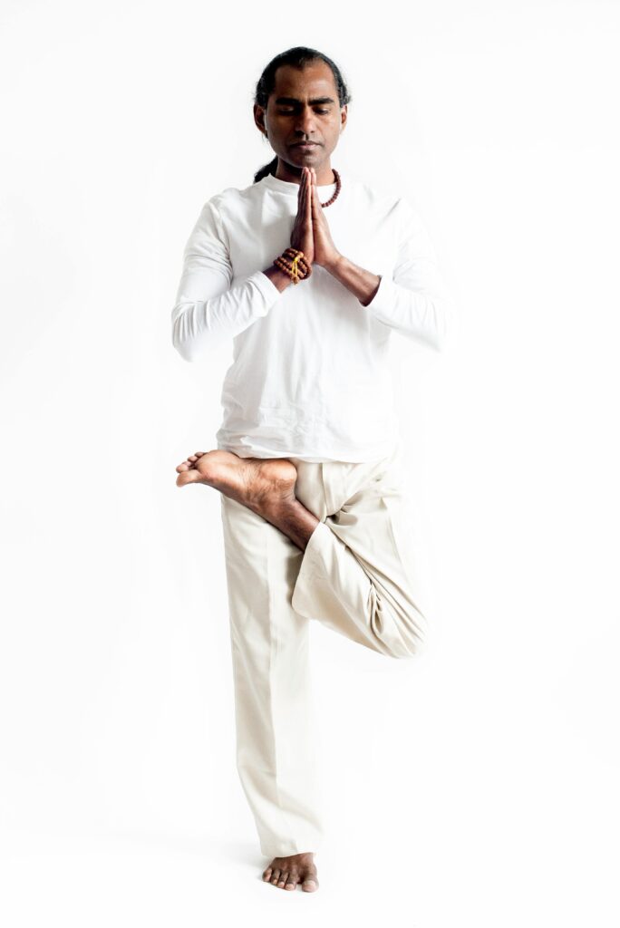 South Asian man practicing yoga in tree pose, exhibiting calm and focus.